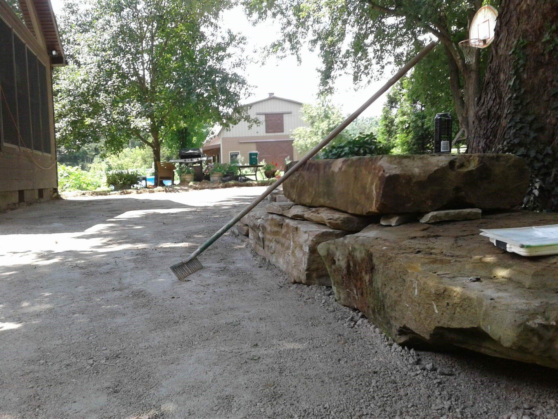 Gravel path beside stacked stone steps under trees, with a house in the background