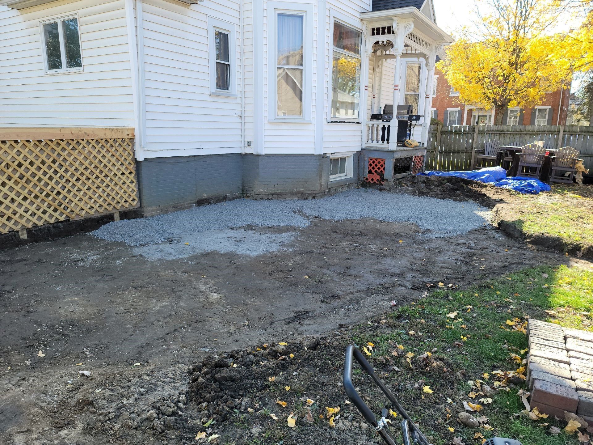 Backyard beside a white house, with a newly cleared dirt area and scattered construction materials