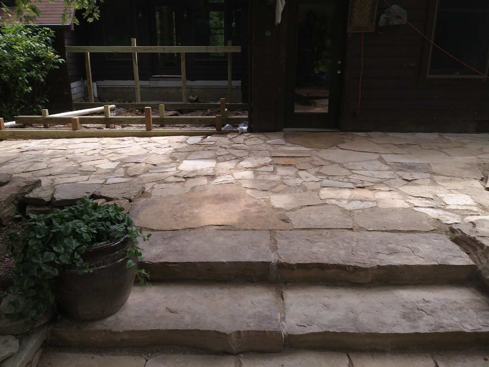 Stone patio with three steps leading to a shaded garden seating area and wooden bench