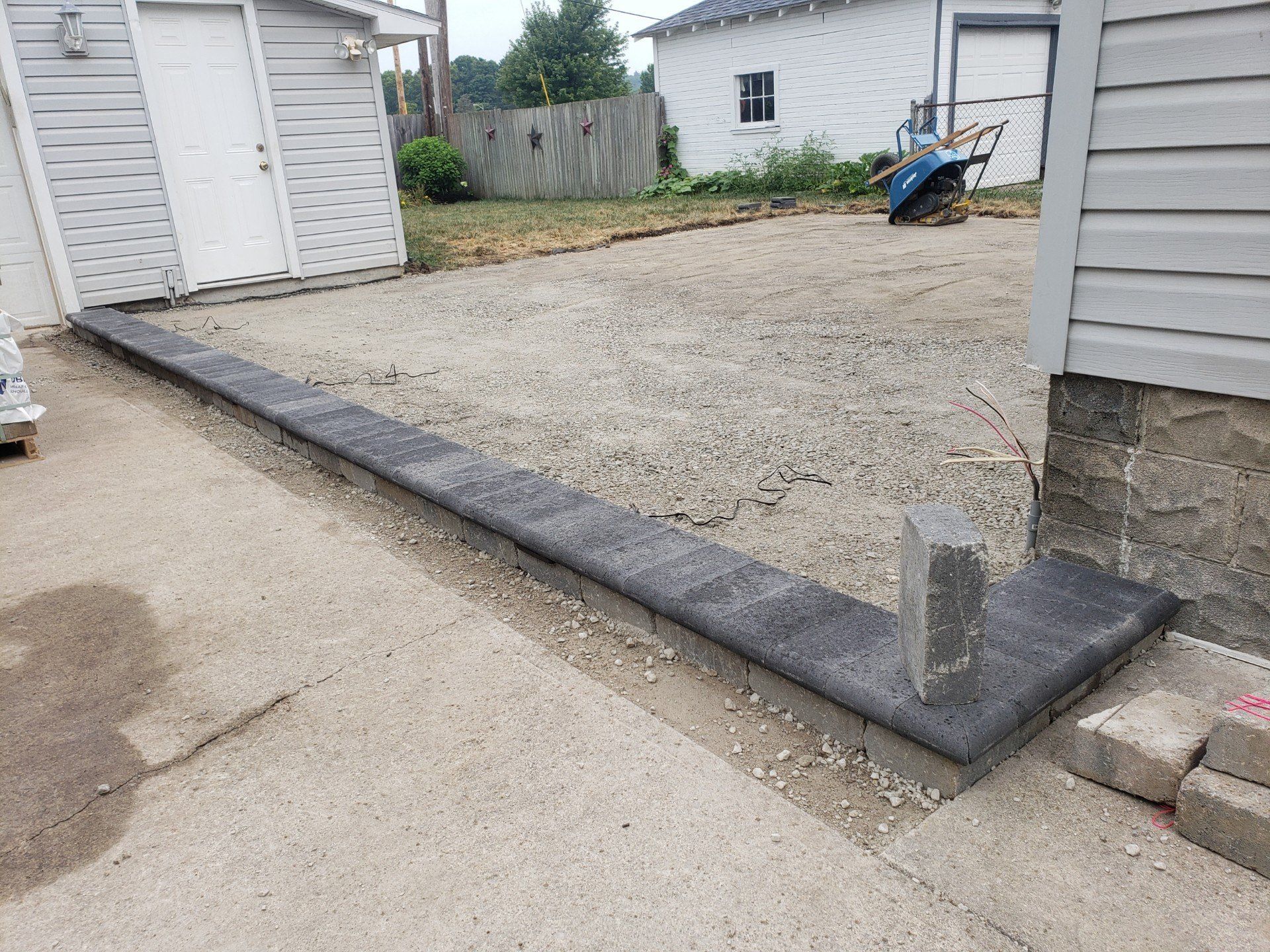 Gravel driveway beside a gray garage with a low curb and a small concrete post at the corner.