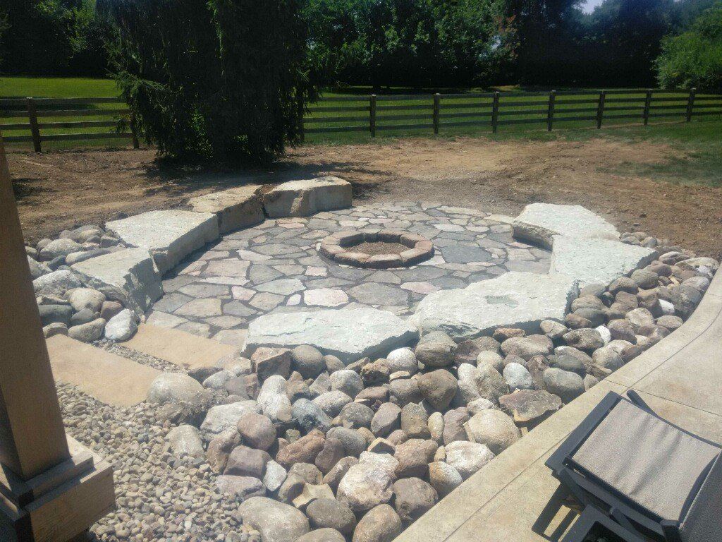 Stone fire pit surrounded by rocks in a grassy yard with a wooden fence in the background.
