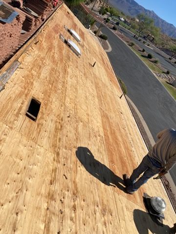 Worker on a sloped plywood roof under construction, with tools and a paved lot below.