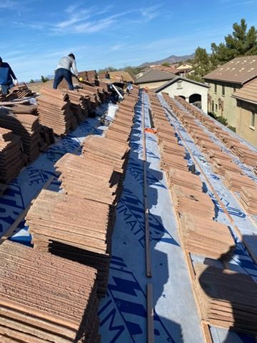 Roofers installing clay tiles on a house roof under a sunny sky.