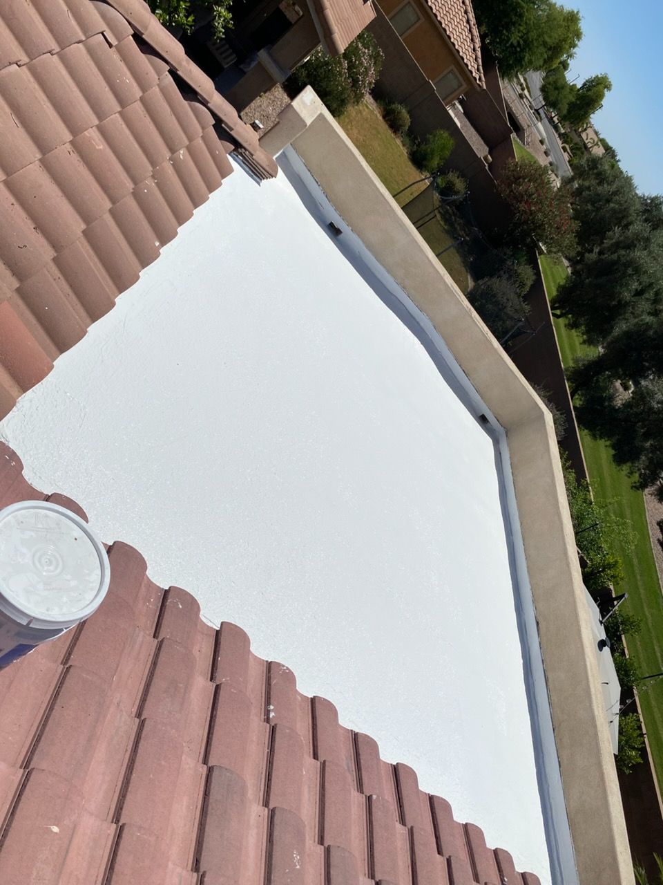Rooftop view of a large white tent canopy beside red tile roofs and a driveway, with trees in the background