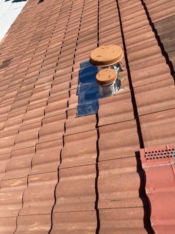 Rooftop with red tiles and a small metal vent capped in tan near the center.