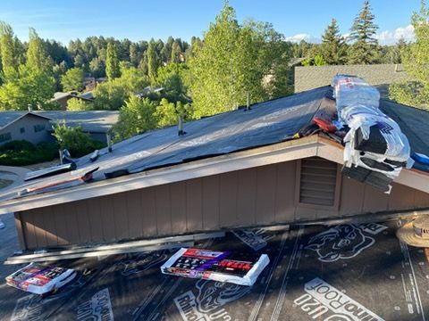 Collapsed roof with workers’ supplies on top of a house in a wooded neighborhood