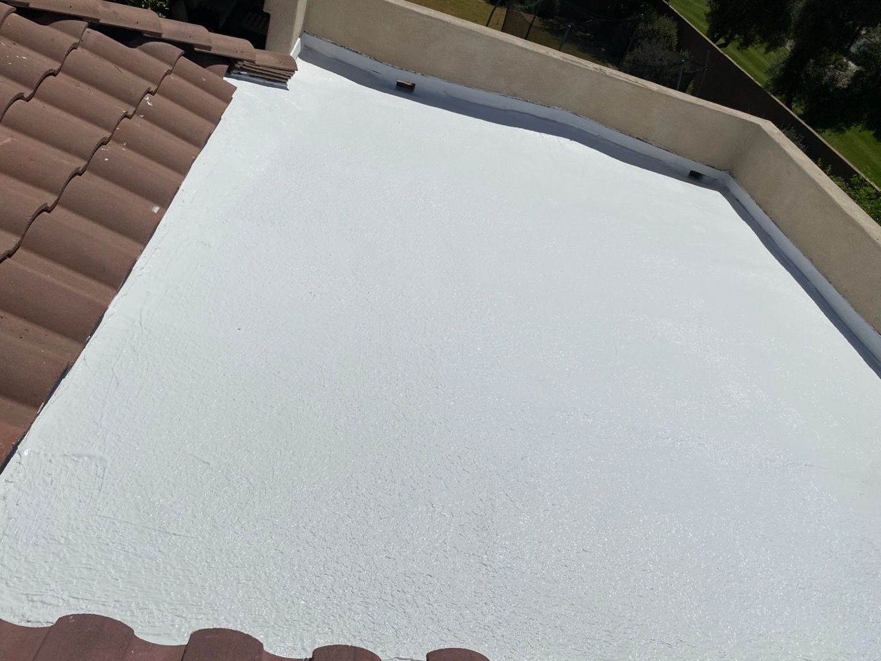 White rooftop membrane beside brown tile roof, viewed from above.