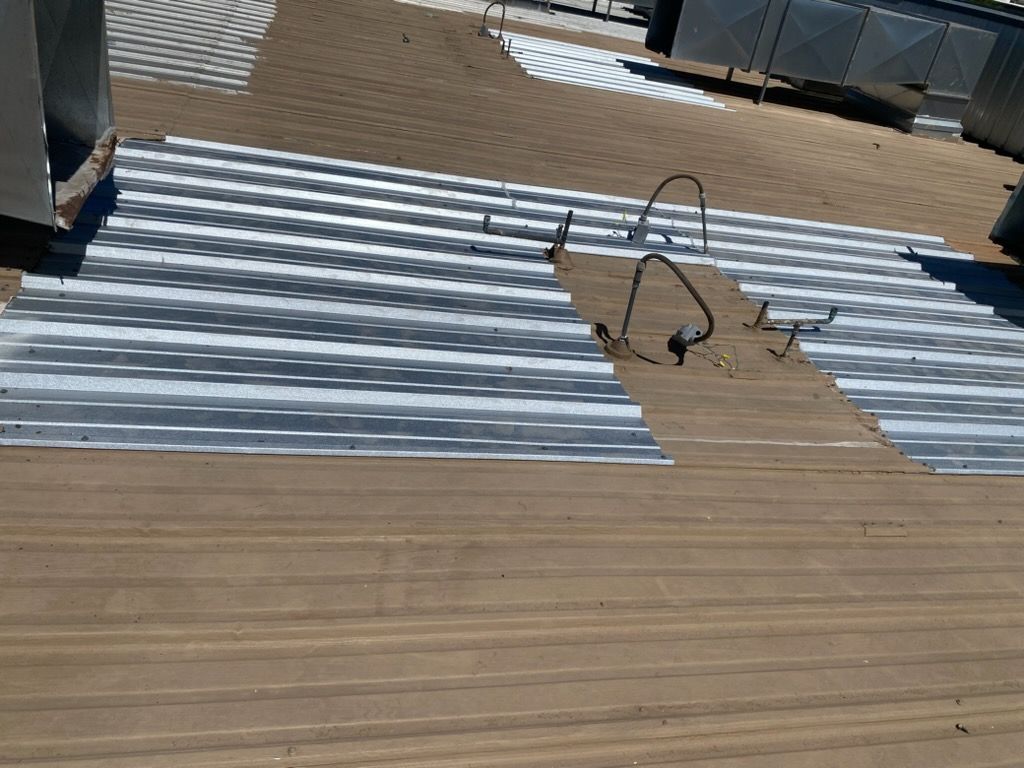 Corrugated metal sheets laid on a wooden rooftop deck with tools and railing in the background
