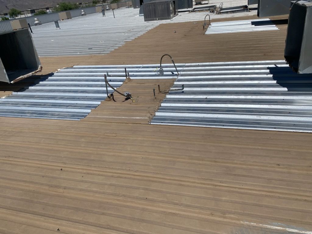 Rooftop with corrugated metal panels, a wooden deck, and pipes near the center opening.