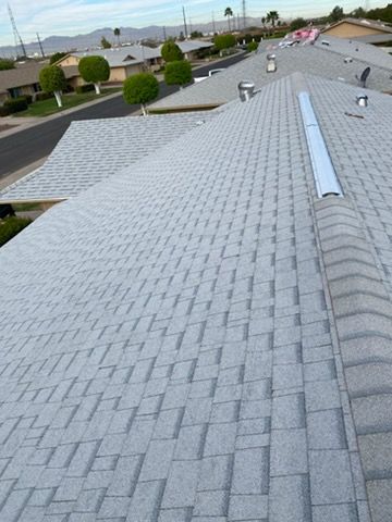 Gray shingled roof with a vent and skylight, overlooking a residential street with trees.