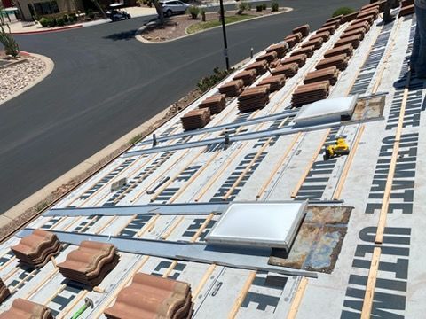 Roof under construction with white beams, brown roofing materials, and tools beside a road