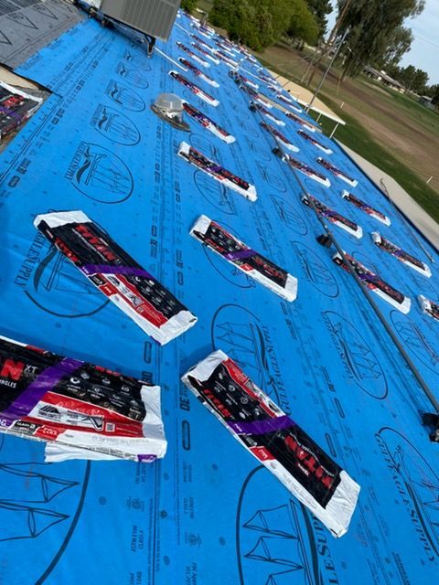 Roof underlayment covered in blue protective material with packages of shingles staged for installation.