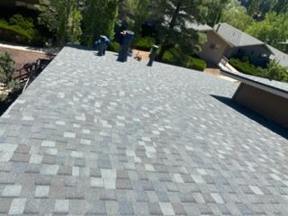 Rooftop with gray shingle roof, two vents, and trees and houses in the background
