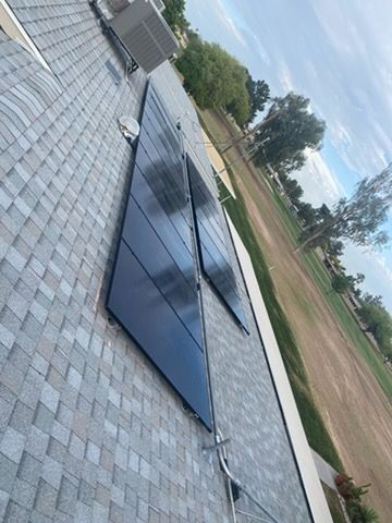 A view looking down a shingled roof showing two rectangular arrays of black solar panels next to an air conditioning unit.