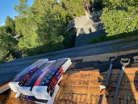 Roofing materials and tools on a sloped roof with trees in the background.