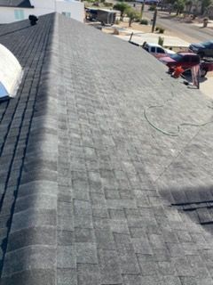Gray shingled roof of a building with a skylight. A person is working on the roof.