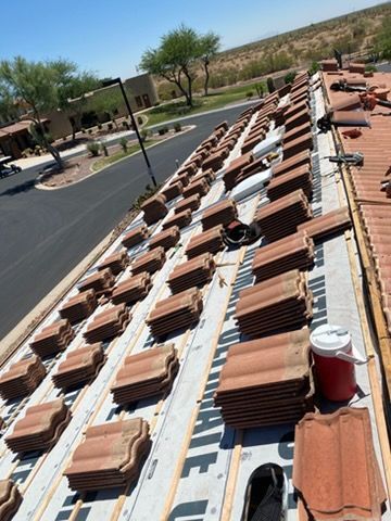 Roof under construction with stacked red tiles and white vents under a bright blue sky
