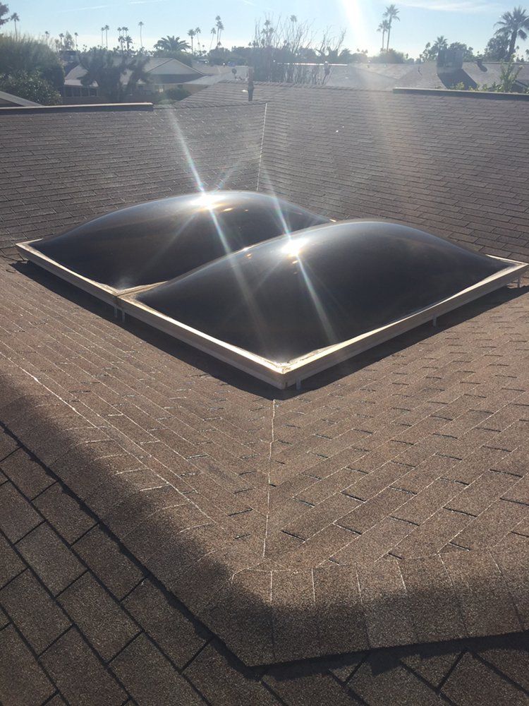 Two dark dome skylights on a brown shingle roof, sunny day.