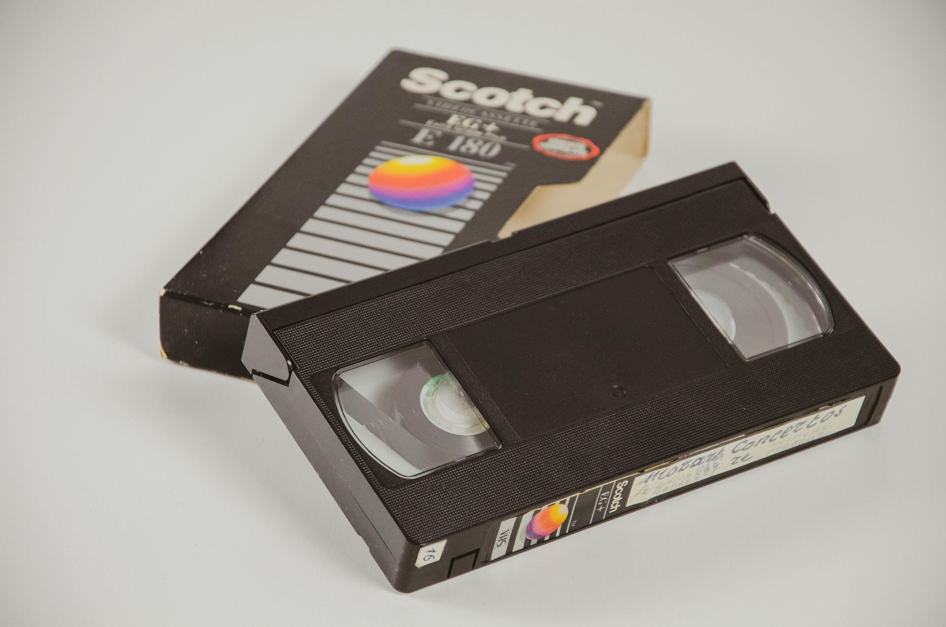 Cassette VHS noire et boîte avec étiquette « Scotch » sur fond blanc.
