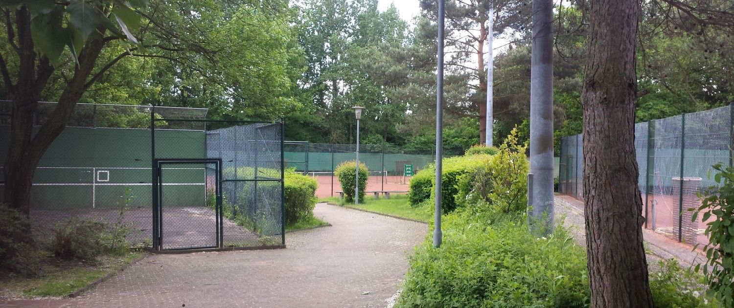 Ein Weg, der zu einem von Bäumen und Büschen umgebenen Tennisplatz führt.