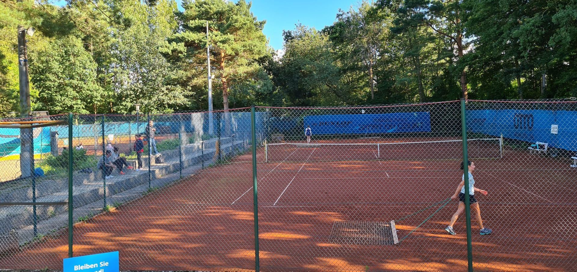 Eine Frau spielt Tennis auf einem Tennisplatz hinter einem Zaun.
