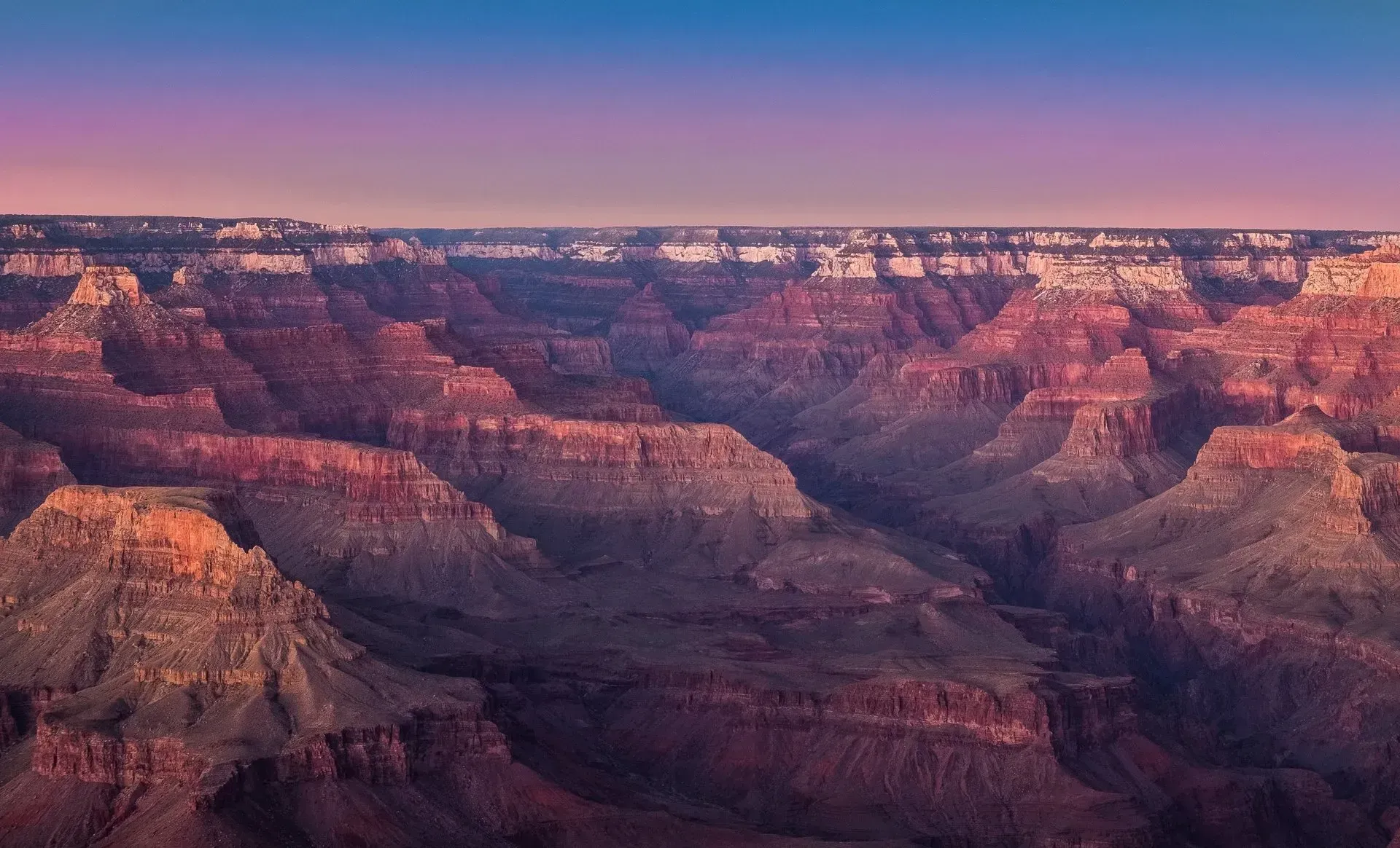 Grand Canyon at sunset, layers of red and purple rock formations beneath a colorful sky.
