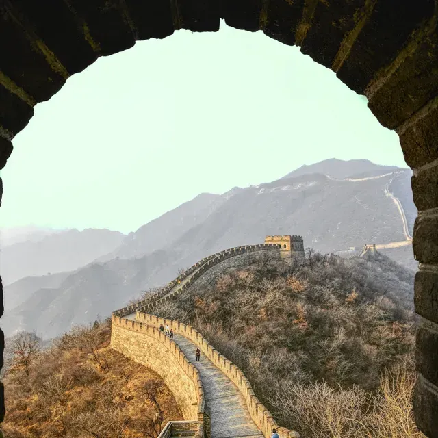 The Great Wall of China winds along a mountain ridge, viewed through a stone archway.