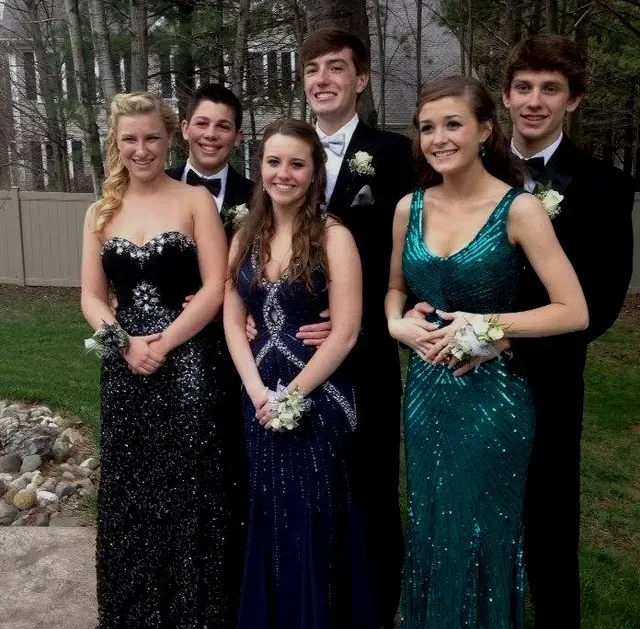 Group of six teens in formal attire, posing outdoors with smiles.