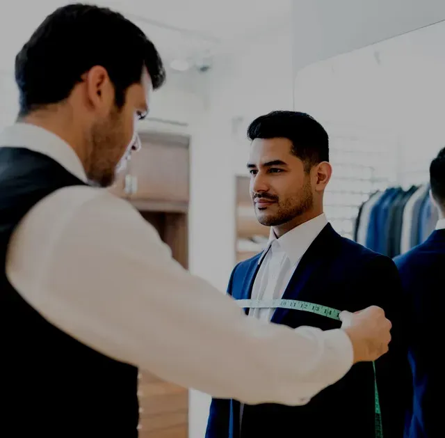 Tailor measuring a man's chest with a tape measure in a suit shop.