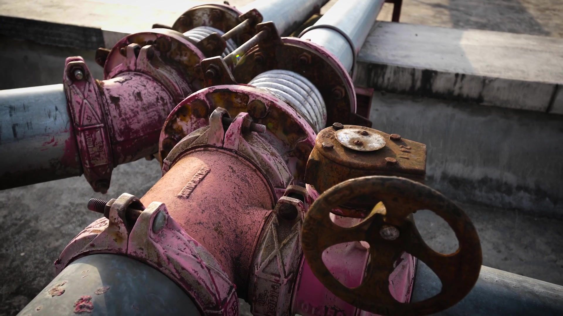 Rusty red fire hydrants and large pipes with valves beside a concrete canal.