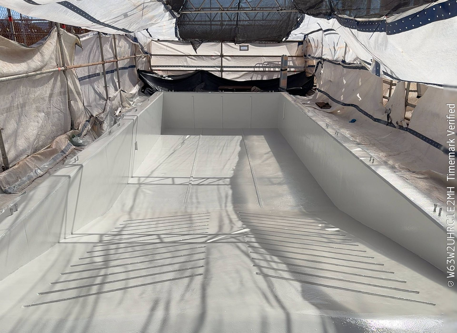 Snow-covered ski slope under protective netting with groomed tracks and a snowy mountain backdrop