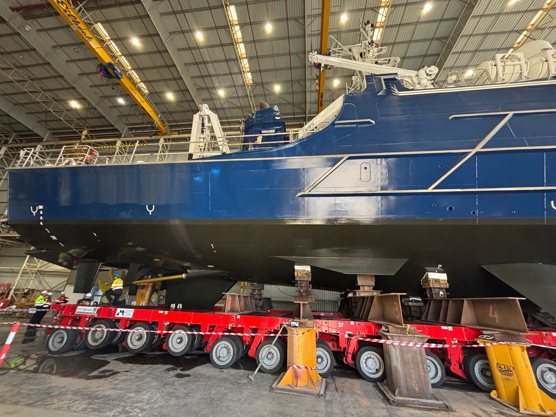 Blue ship hull resting on red transport modules inside a large industrial hangar