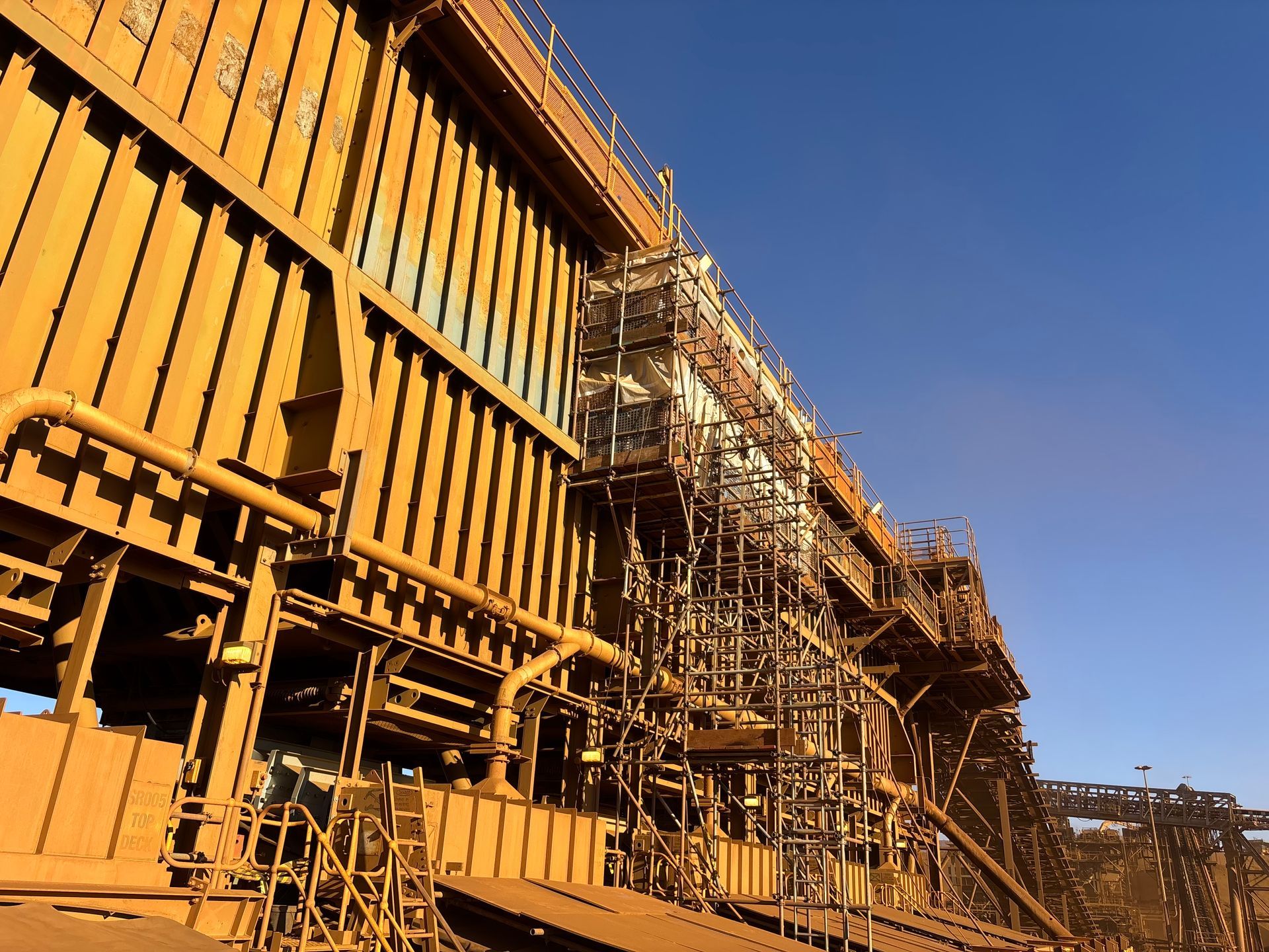 Orange industrial structure under construction against a clear blue sky