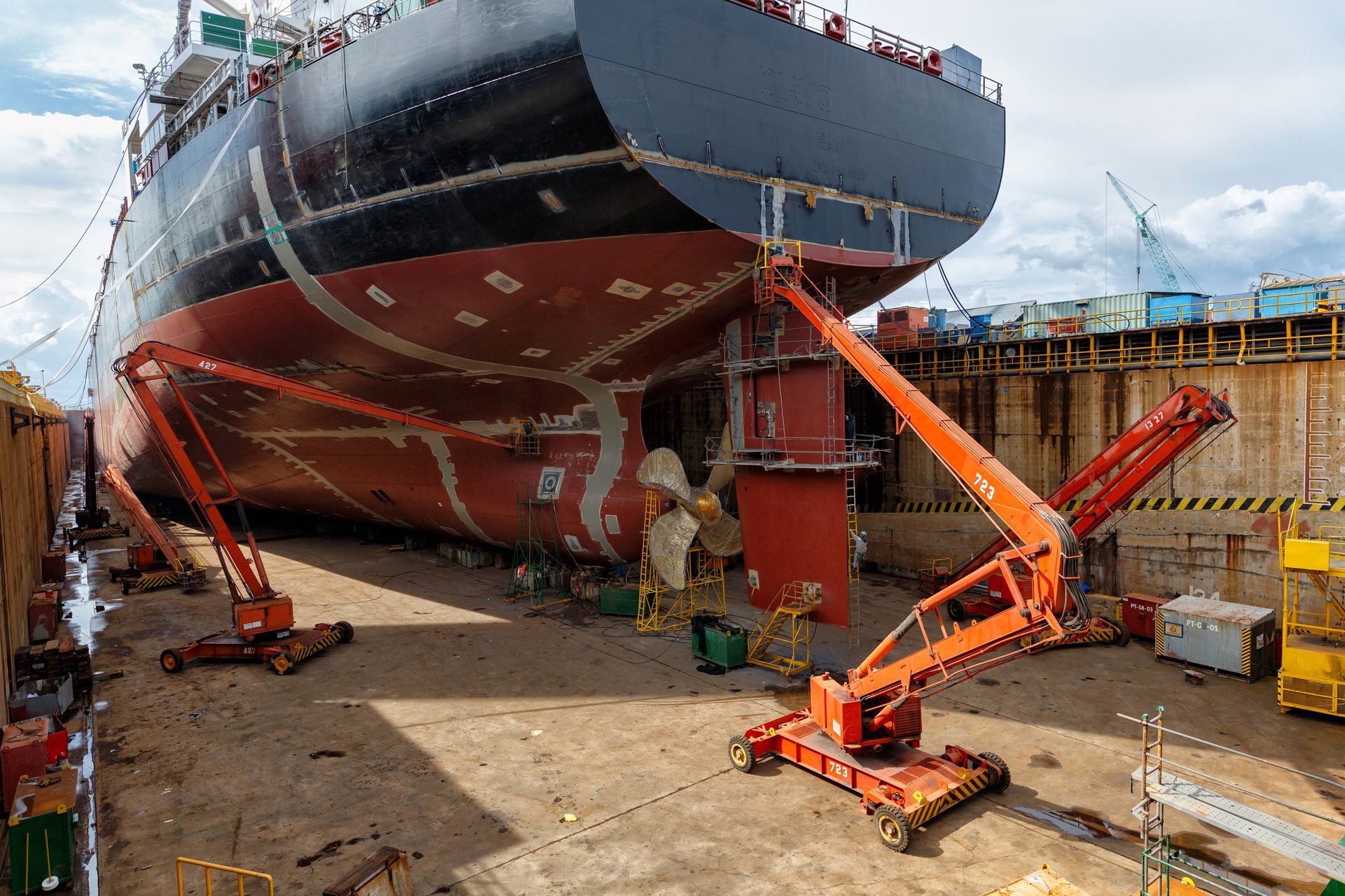 Huge ship in dry dock with workers and orange support scaffolds under the hull