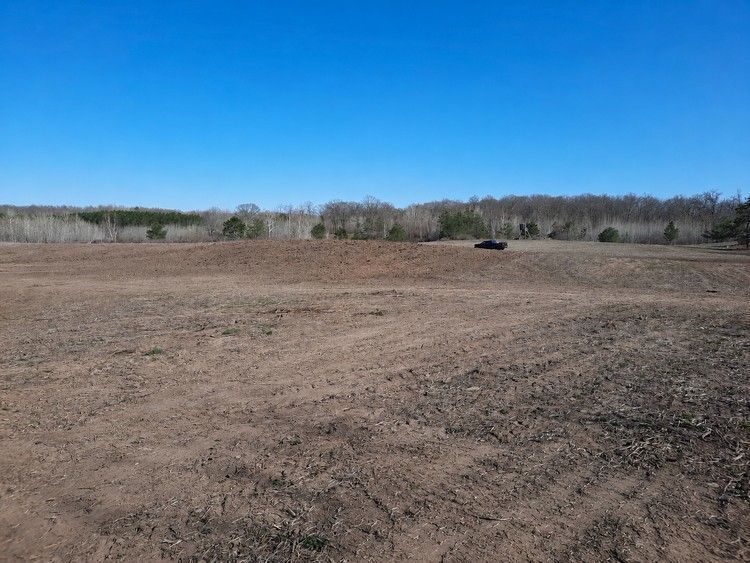 Open dirt field under a clear blue sky, with a tree line in the distance.