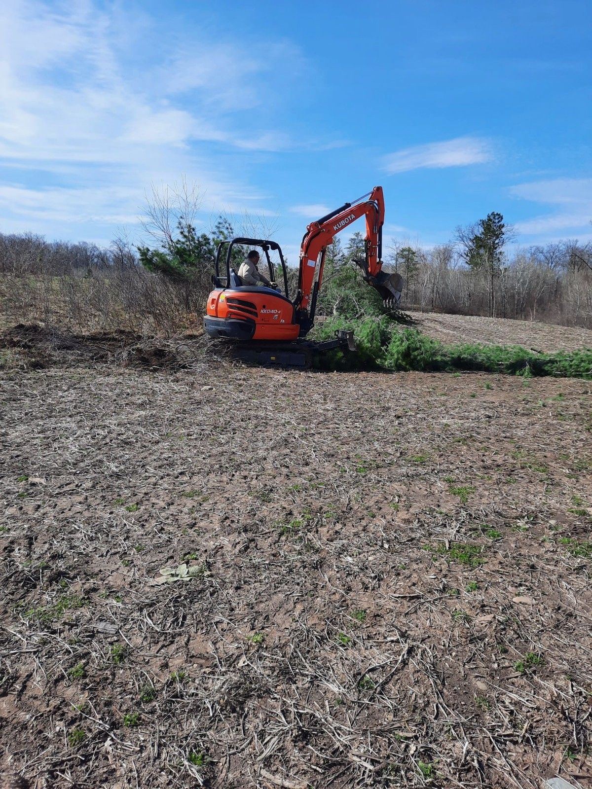 Orange excavator clearing brush in a dry field under a blue sky