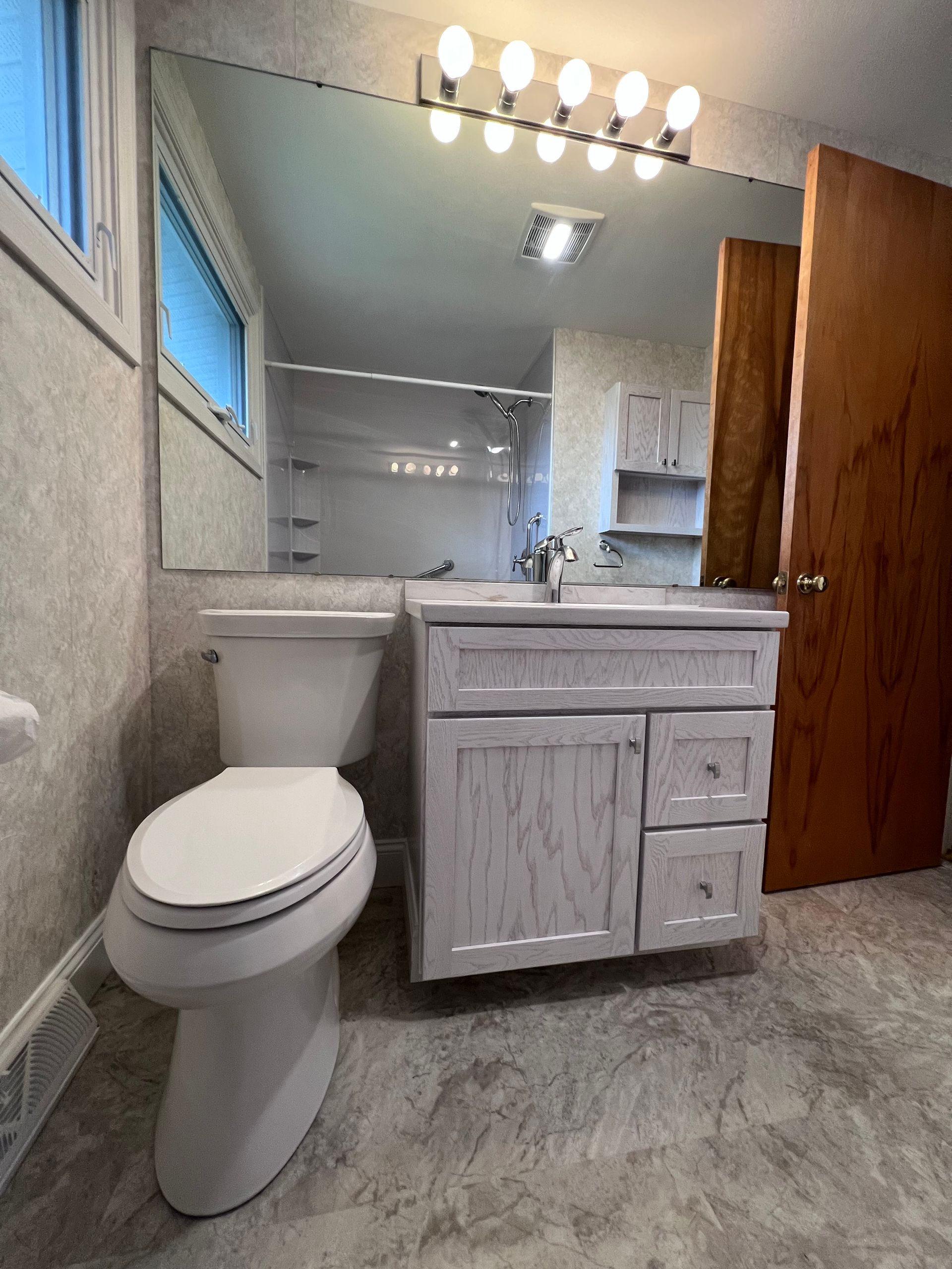 Small bathroom with toilet, white vanity, mirror, lights, and wood door.
