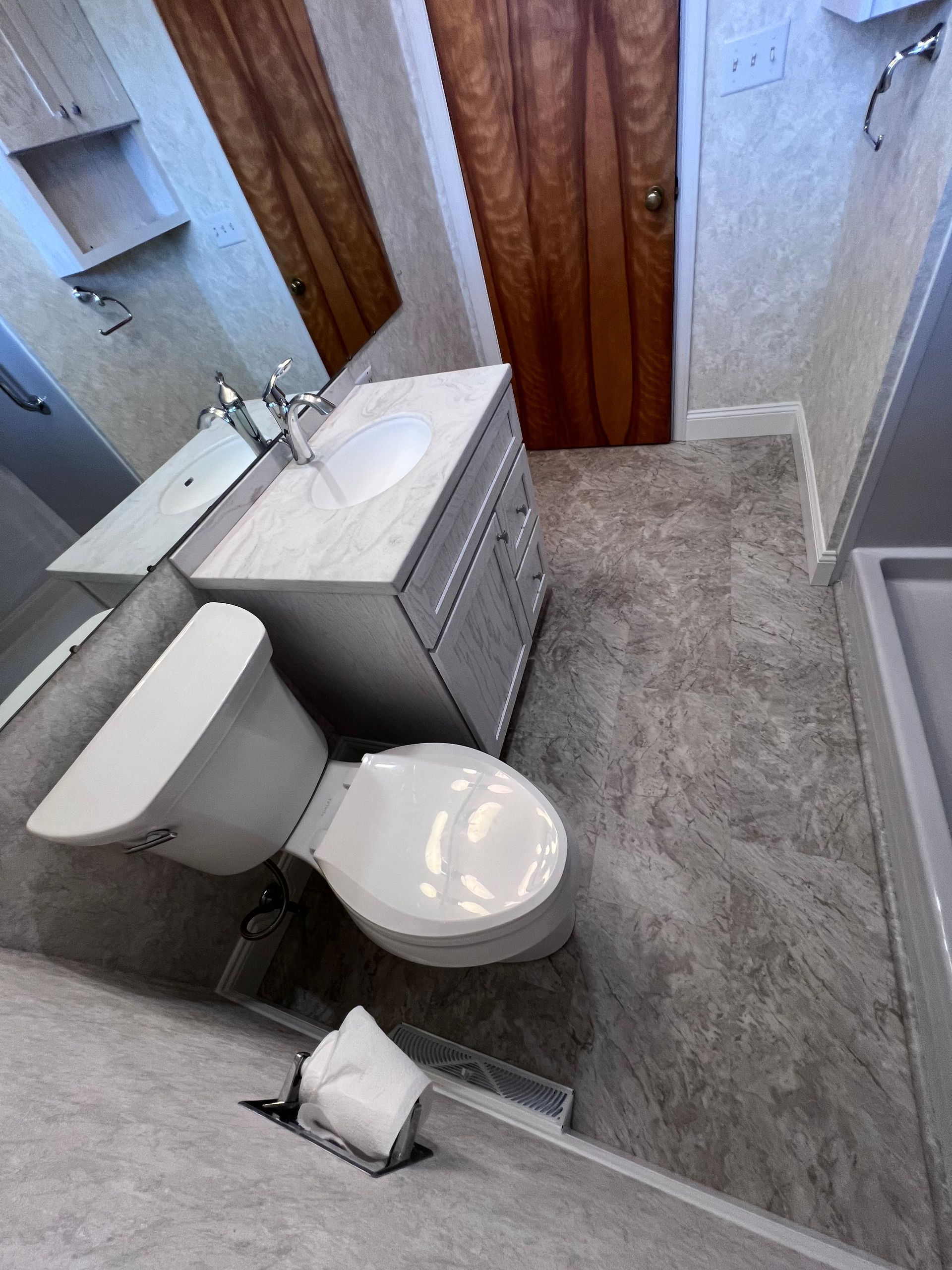 Small bathroom with toilet, sink vanity, shower stall, and gray floor tiles.
