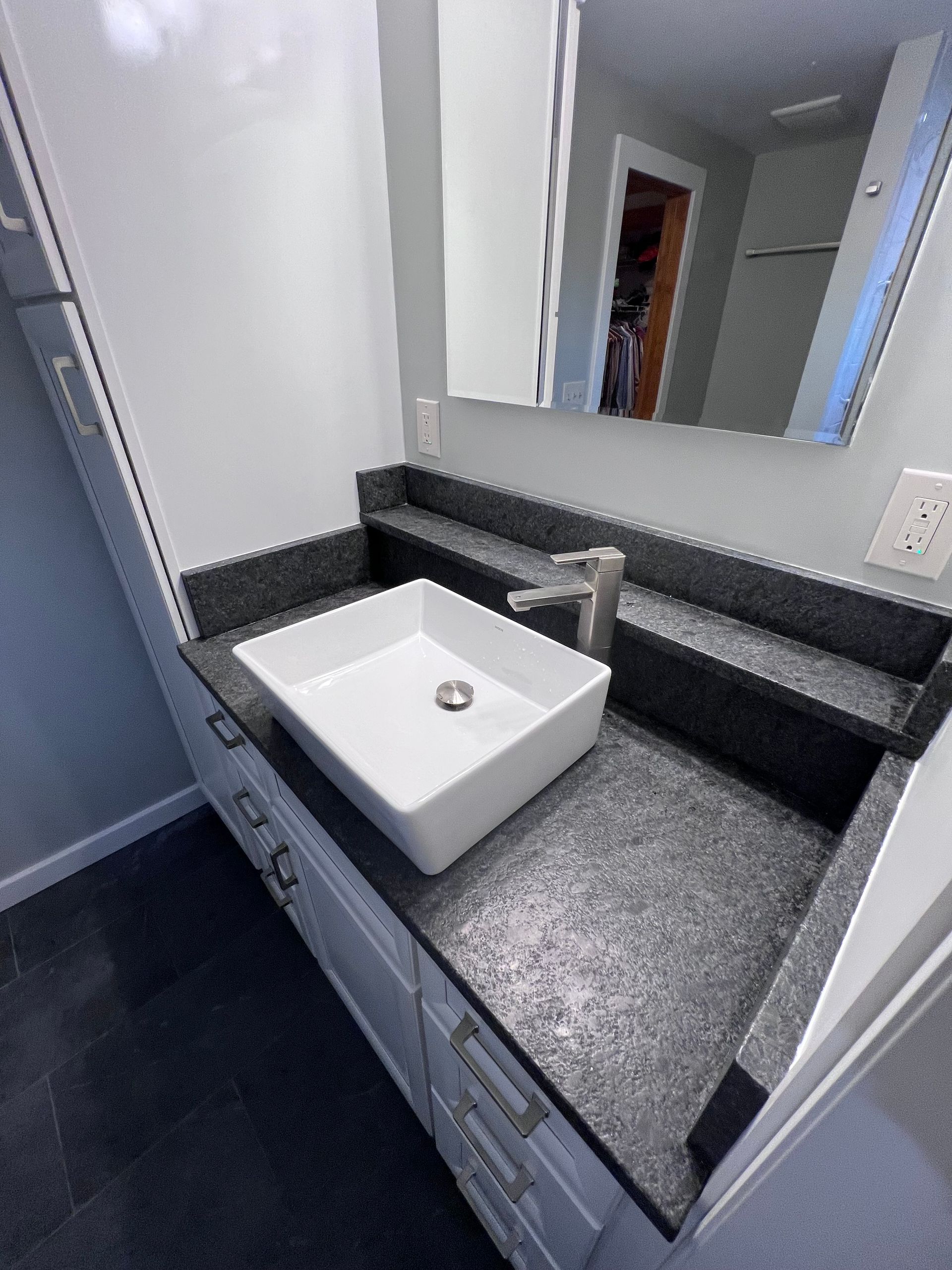 Bathroom vanity with white vessel sink, dark speckled countertop, and large mirror above.