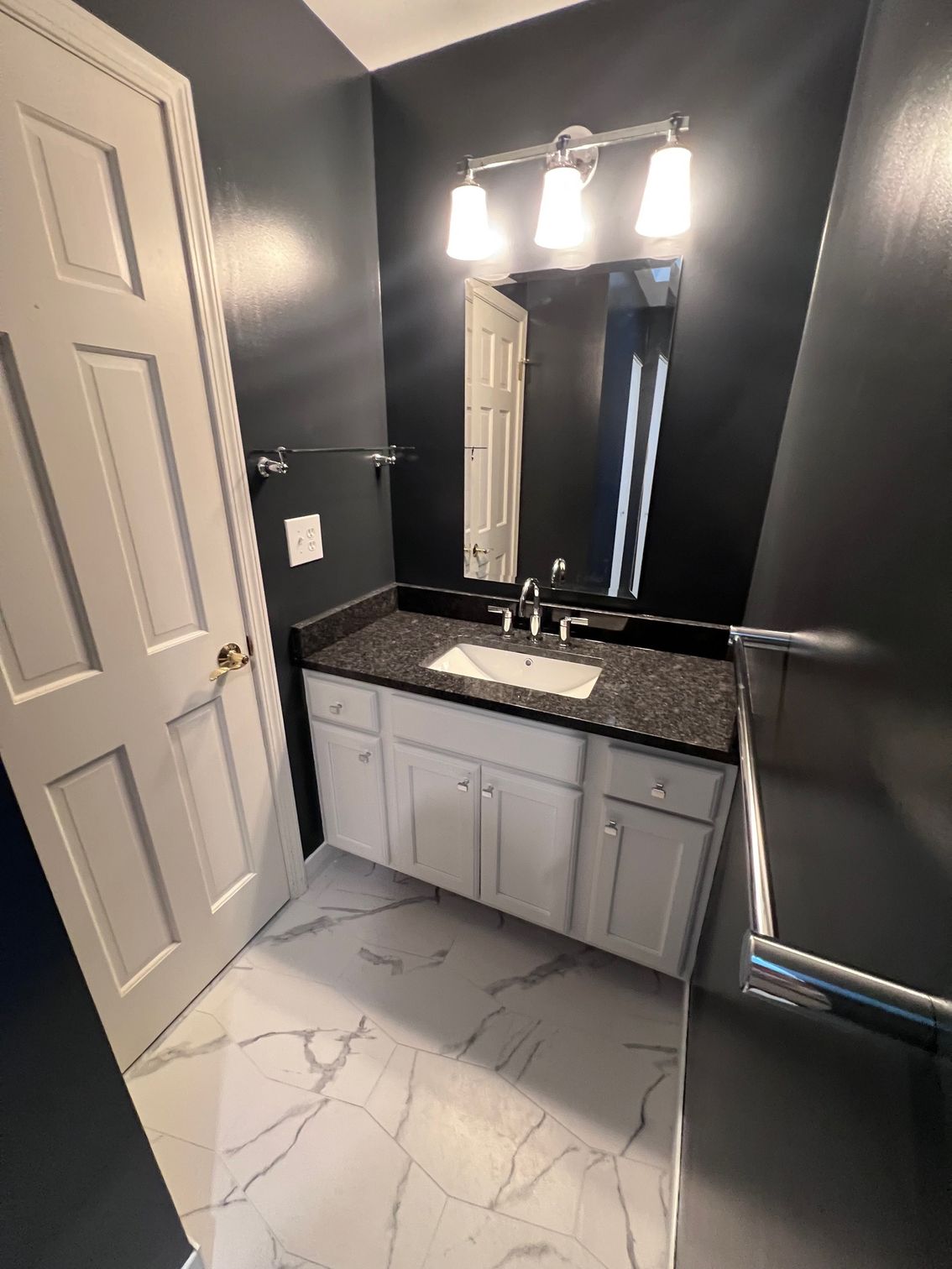 Small bathroom with dark walls, white vanity, mirror lights, and marble-look floor and countertop.