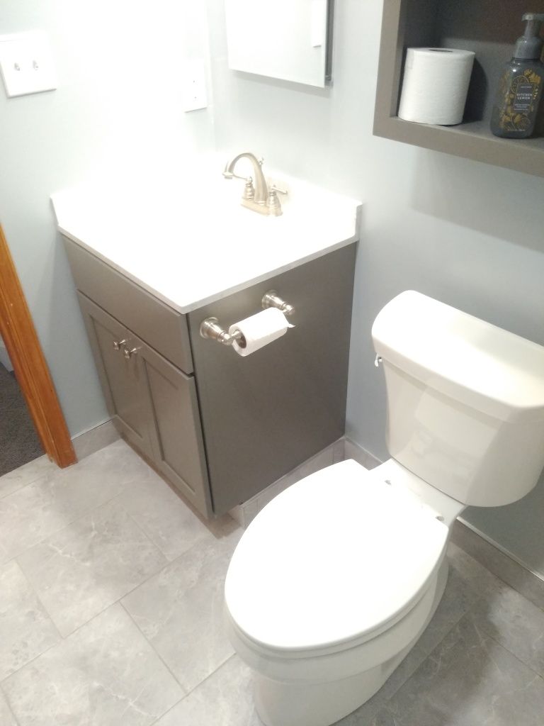 Small bathroom with white toilet, gray vanity cabinet, and towel holder under a wall mirror.