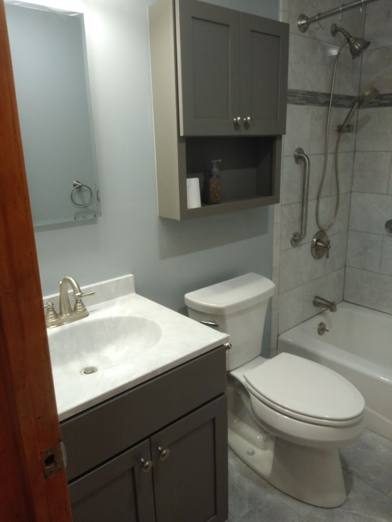 Small bathroom with sink, toilet, bathtub, mirror, and gray cabinets.