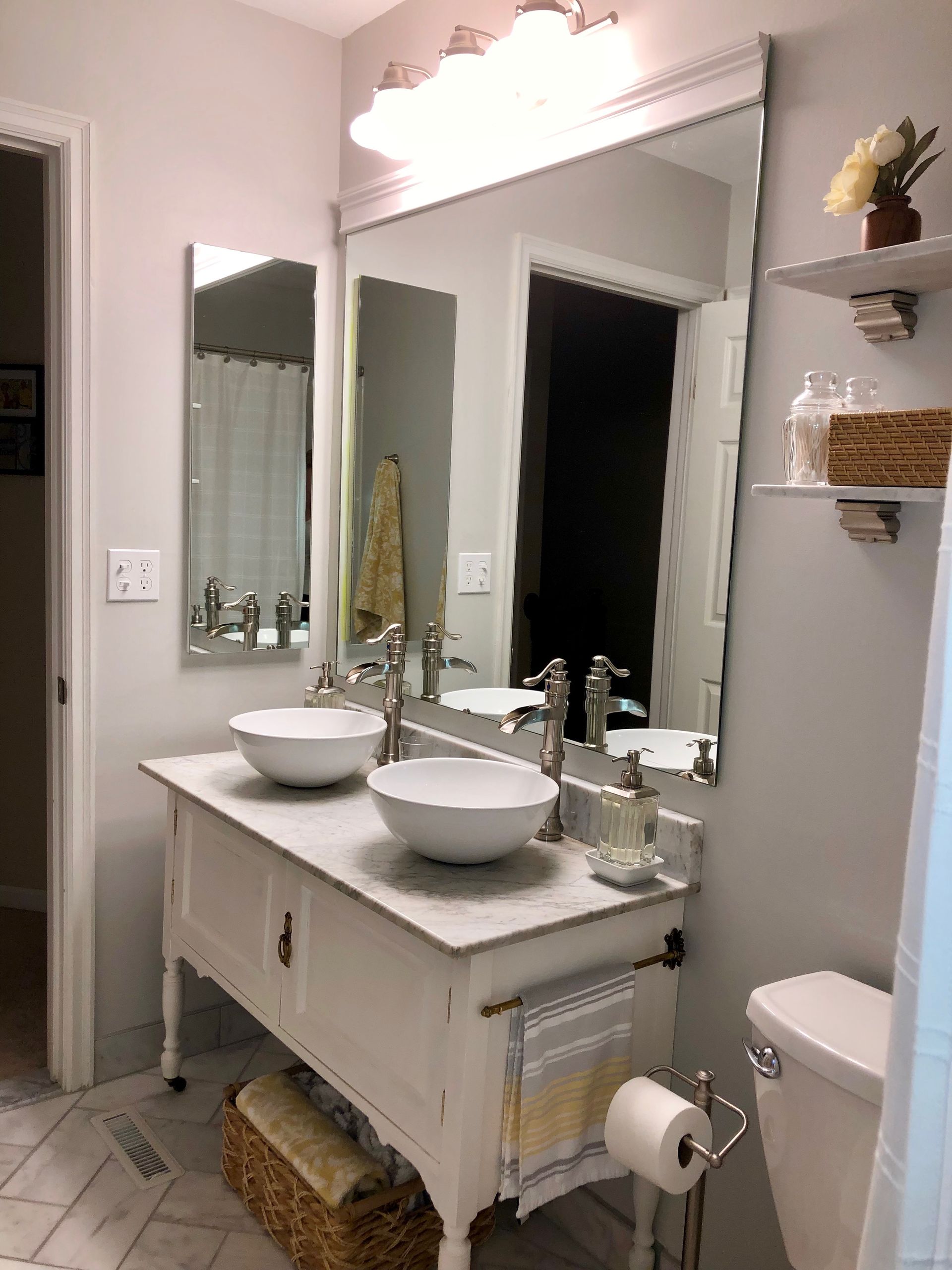 Bathroom vanity with twin sinks, large mirror, and light pink walls, with shelves and towels nearby