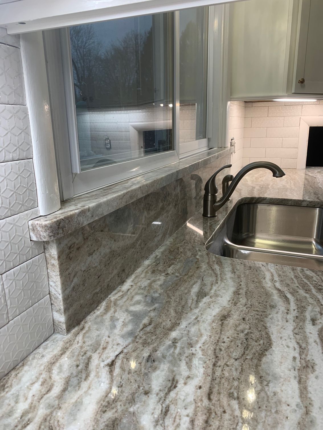 Kitchen countertop with gray marble pattern, stainless sink, curved faucet, and window above the counter