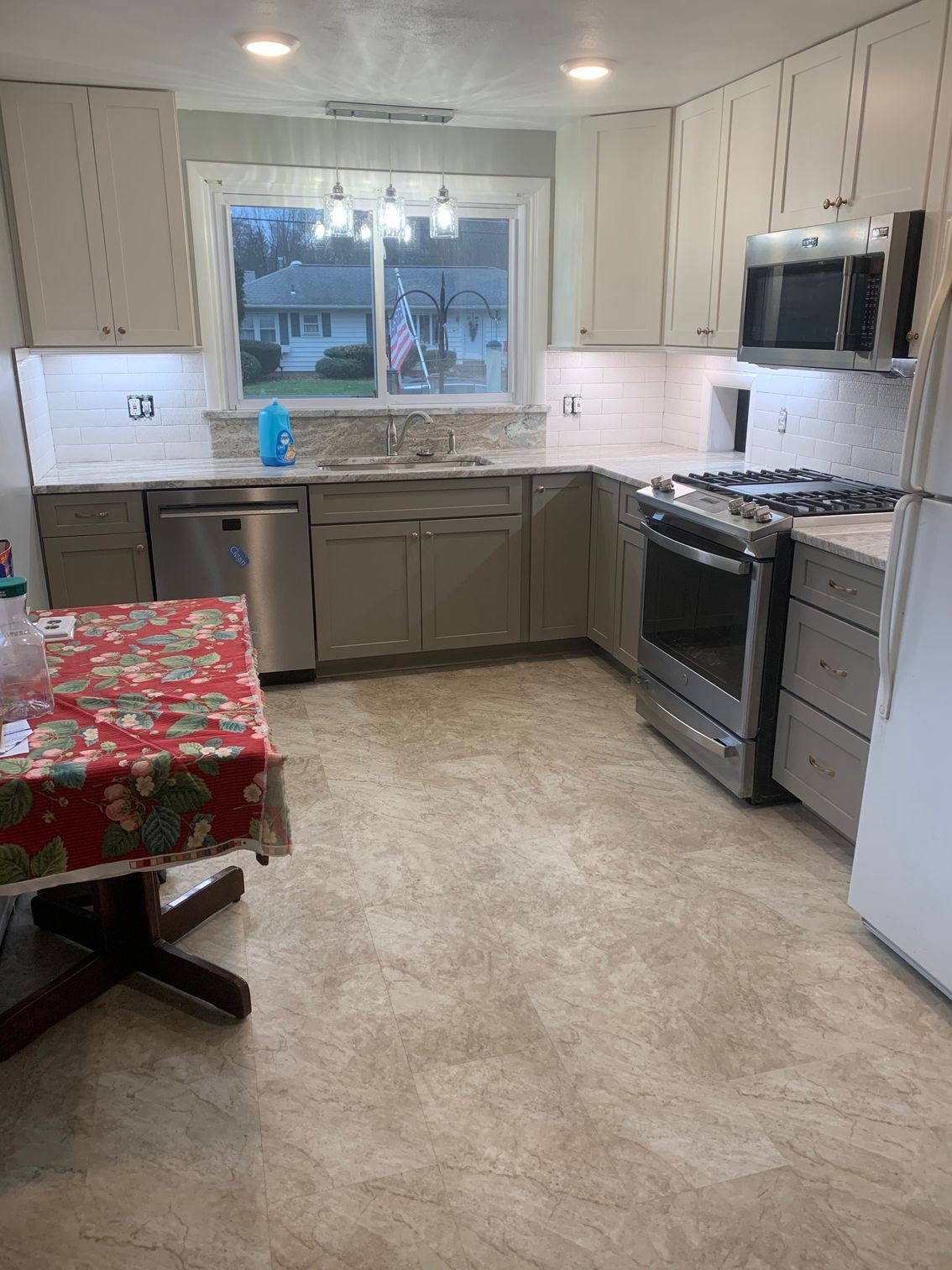 Small kitchen with white cabinets, stainless appliances, a window over the sink, and a red tablecloth on the table.
