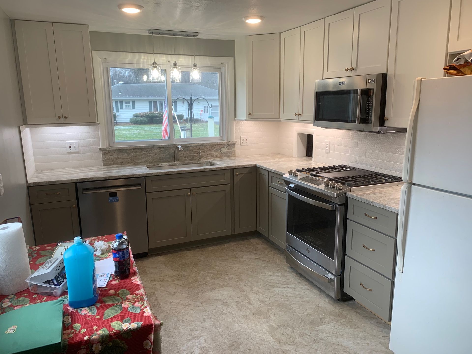 Bright kitchen with white cabinets, gray lower cabinets, stainless appliances, and a window over the sink.