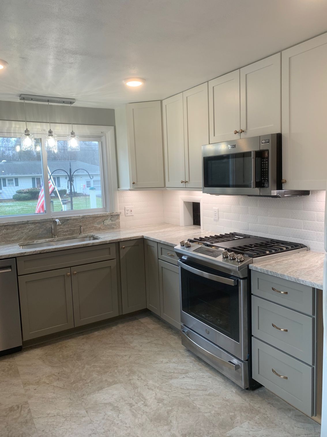 Bright kitchen with white cabinets, gray lower cabinets, granite counters, and stainless steel stove and microwave.
