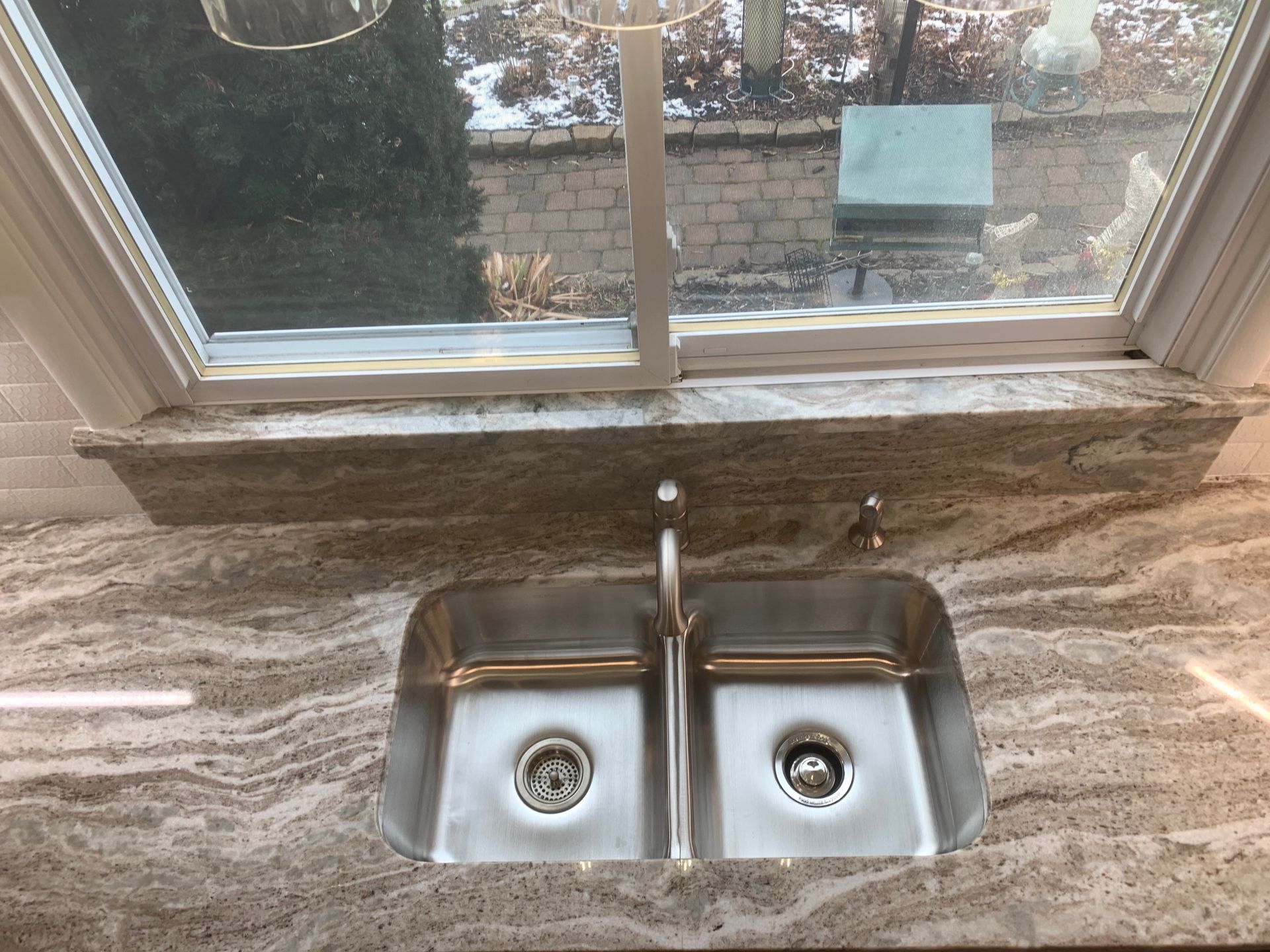 Stainless steel double sink under a window with granite countertop and outdoor view