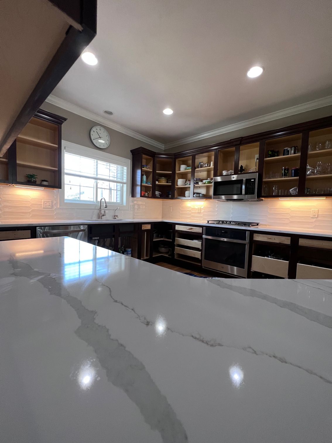 Modern kitchen with white marble island, dark wood cabinets, stainless appliances, and recessed lighting