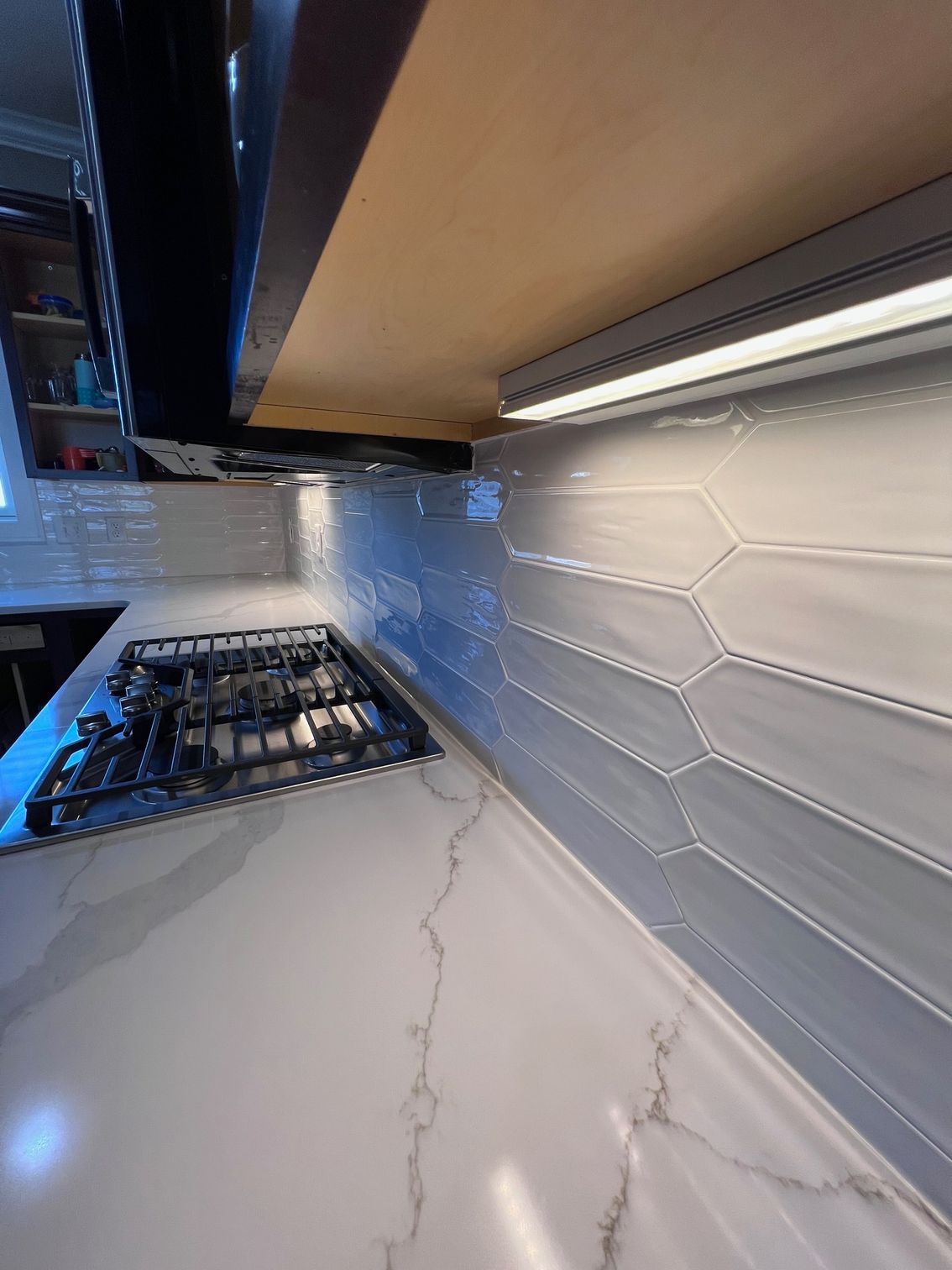 Modern kitchen countertop with white marble look, gas stove, and white hexagon-tile backsplash under under-cabinet light